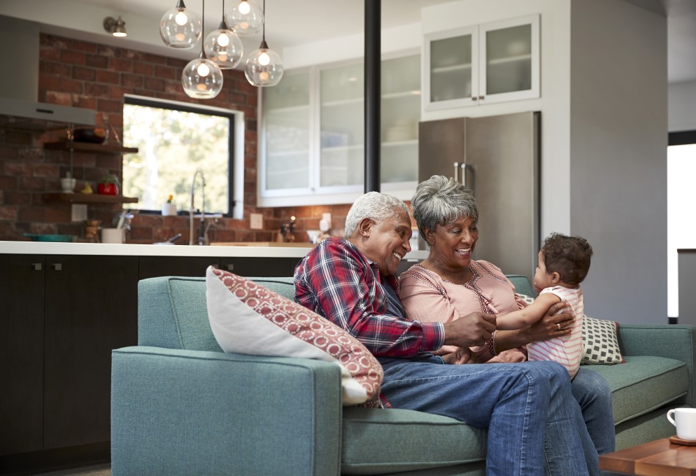 A Black grandmother and grandfather smile at their baby granddaughter as the grandmother holds her