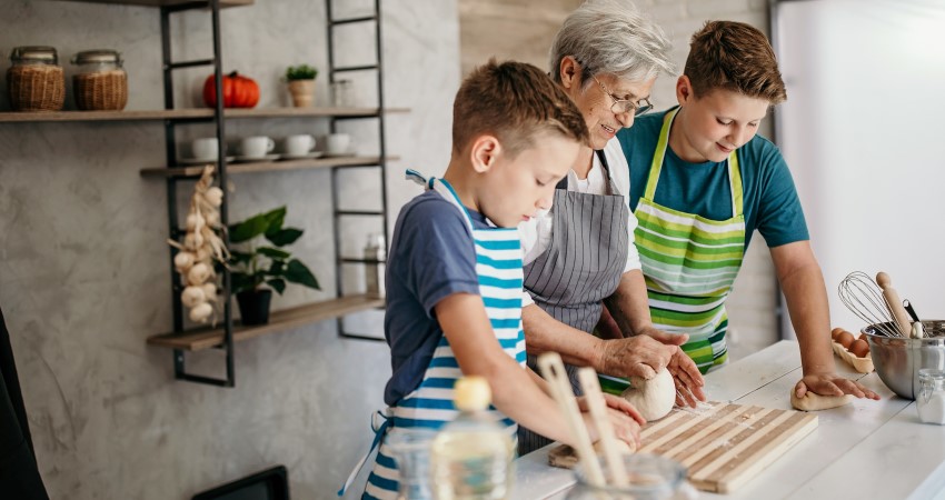 A white grandmother and her two grandsons work on dough together in the kitchen