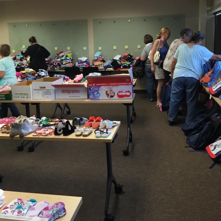 Caregivers look at items in a room with socks, shoes, backpacks, and other necessities organized and laid out on tables for them to select.
