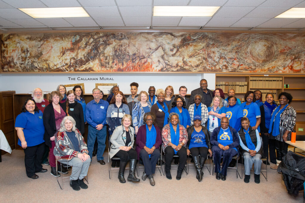 A diverse group of people, mostly women, pose for a photo together.