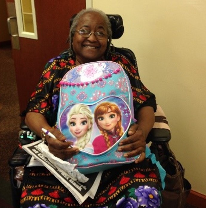 An African American grandmother in a wheelchair smiles as she holds a backpack featuring characters from the movie Frozen
