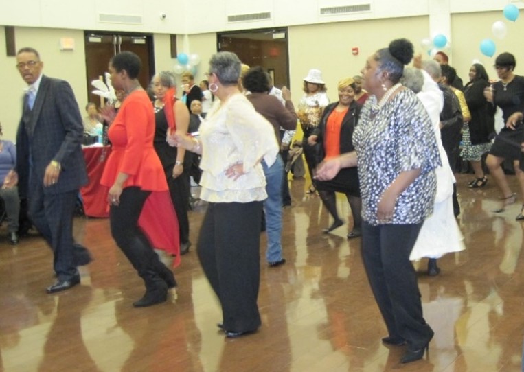 A group of caregivers, primarily older Black women, dance during an event
