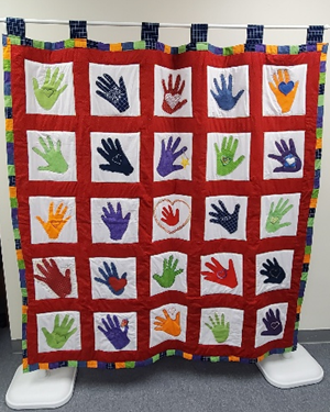 Photo of a colorful quilt with a handprint in each square