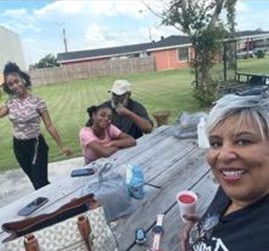 A Black kinship family - grandmother, grandfather, and two preteen/teenage girls - is all smiles as they gather around a picnic table