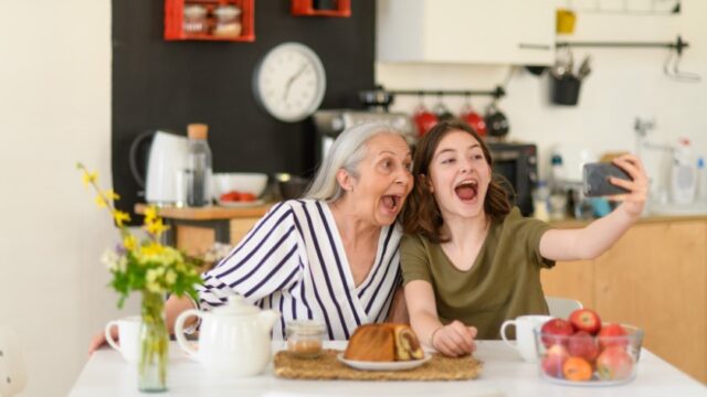 A white grandmother and her granddaughter take a selfie together at the kitchen table