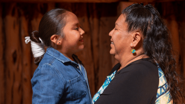 A Navajo grandmother and her young grandson smile as they look at each other