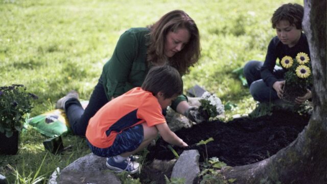 A Native woman gardens with two children