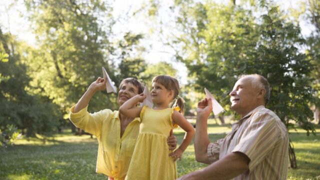 A white grandmother, grandfather, and young granddaughter prepare to throw paper airplanes outside together