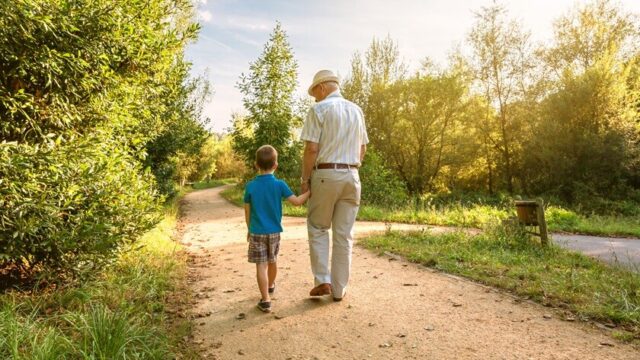 A white grandfather and grandson hold hands and walk along a path