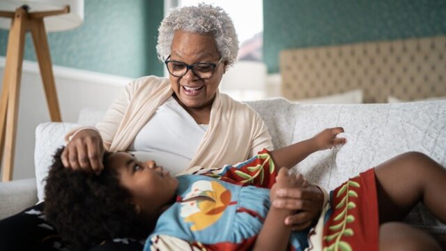 A Black grandmother smiles at her granddaughter. The granddaughter is looking up at her grandmother and has her head in her grandmother's lap
