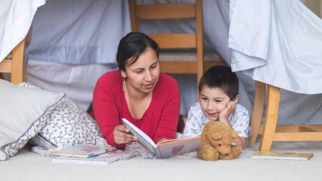A Native American woman and child read together in an indoor blanket fort