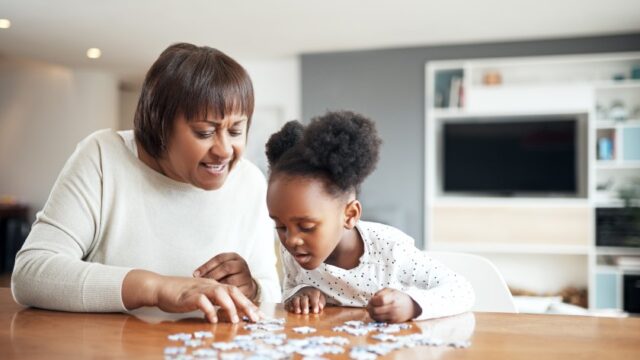 A Black grandmother and her young granddaughter work on a puzzle together