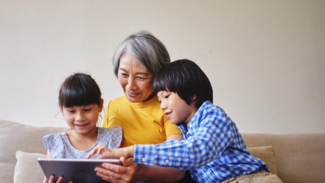 A grandmother and her elementary-aged granddaughter and grandson use a tablet together in a home in Taiwan.
