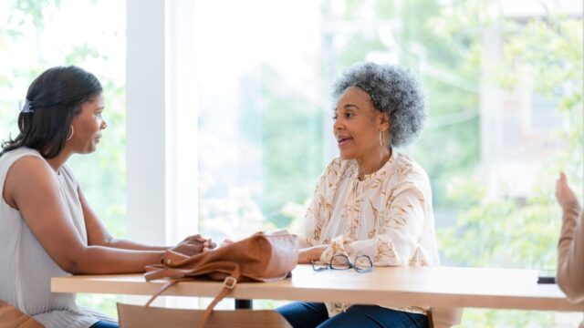 Two Black women sit a table in a coffee shop and talk