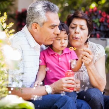 A Latino/Hispanic grandmother and grandfather blow bubbles with their toddler granddaughter