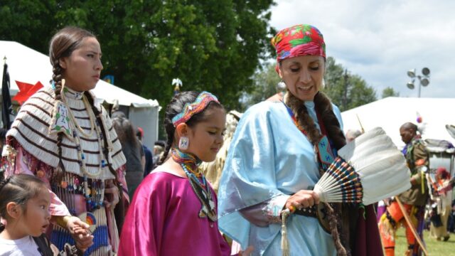 A tribal elder leads young people, and all are dressed in traditional clothes