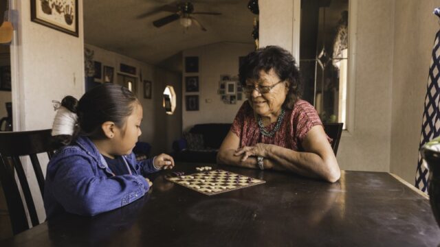 A Native grandmother and her grandchild sit at a table and play a game together.