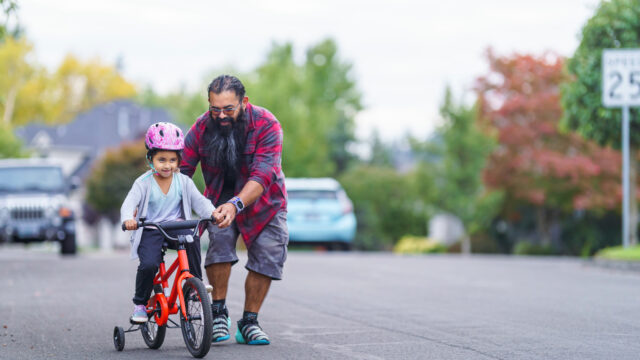 A Native man helps his young relative learn to ride a bike