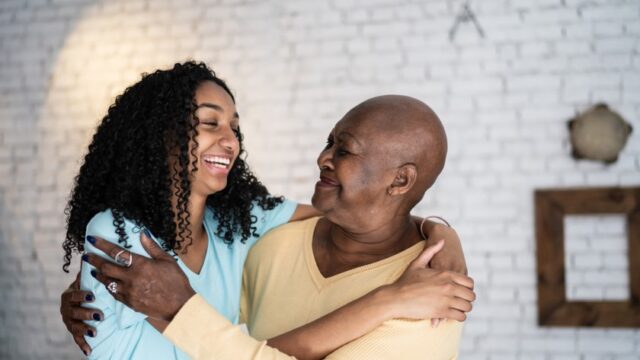 A Black teenager and her grandmother smile at each other as they embrace