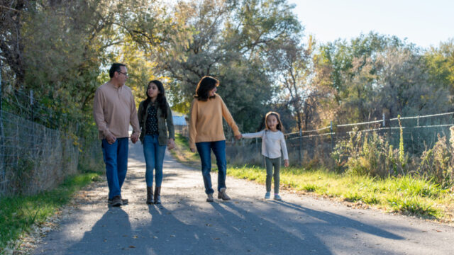 A grandmother and grandfather each holds hands with and looks at one of their granddaughters as the four of them walk down a path together