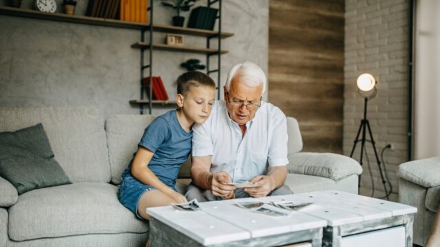 A white grandfather and grandson look at old family photos together.
