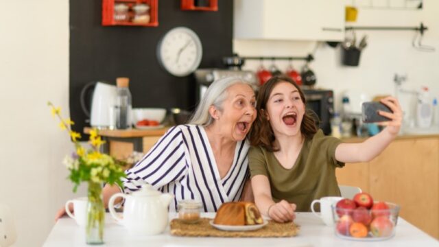 A white grandmother and her granddaughter take a selfie together at the kitchen table