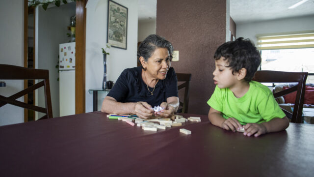 A Latina grandmother and her young grandson sit at a table and play together at home