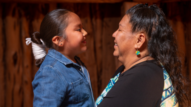 A Navajo grandmother and her young grandson smile as they look at each other