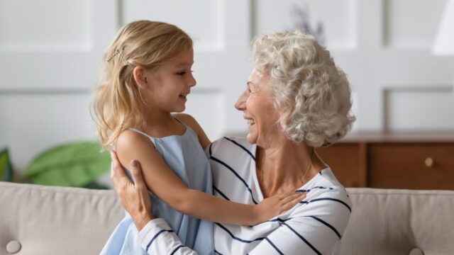 A white grandmother has her arms around her young granddaughter and the two smile at each other