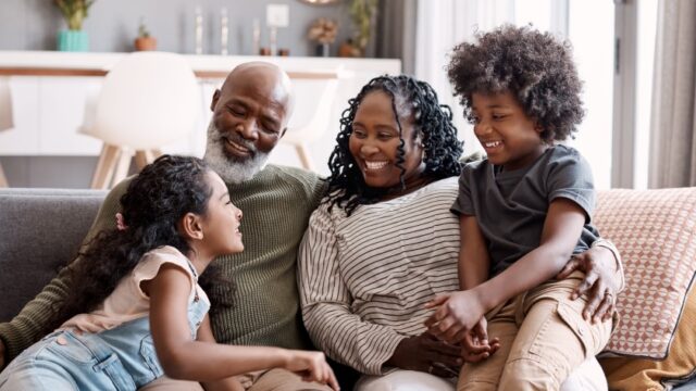 A black family sitting on a couch while smiling and holding each other.