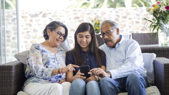 A Latina teenager and her grandmother and grandfather look at a smartphone together