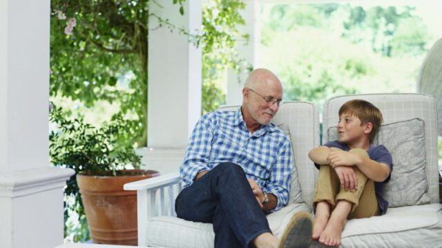 A white grandfather and grandson sit outside and talk to each other