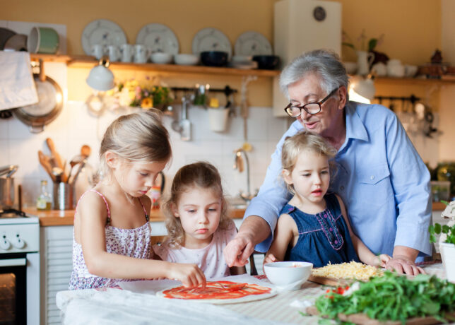 A grandmother helps her three young granddaughters make homemade pizza the kitchen