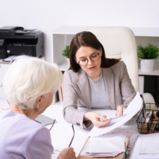 Woman sitting at an office desk showing an older adult documents.